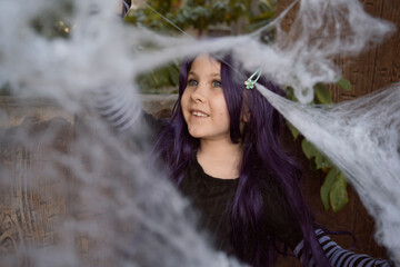 little girl wearing purple wig plays with artificial cobweb - Halloween decoration