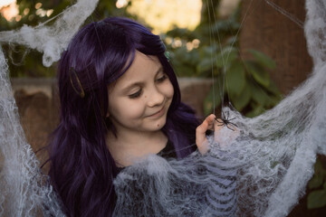 little girl in purple wig plays with artificial spider webs Halloween decorations