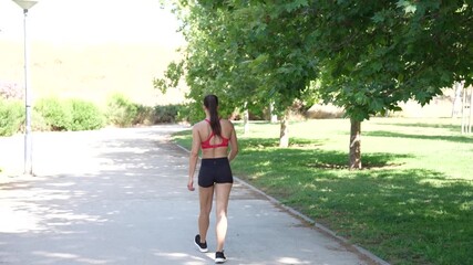 A woman is jogging in the park during summertime, focusing on fitness and outdoor activity