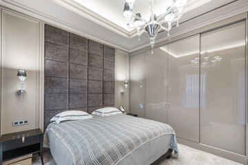 A cozy bedroom showcases a comfortable bed with soft linens, elegant wall accents, and decorative lighting. The space combines modern features with a warm atmosphere, ideal for relaxation.