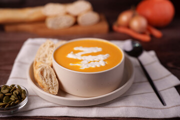 warm and cozy autumn meal: creamy pumpkin soup in beige bowl with bread, seed garnish, spoon on white linen, set against rustic wooden surface with softly blurred vegetables, photography, flavorful