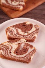 close-up of sliced marble cake on a white plate showcasing intricate chocolate and vanilla swirls with a wooden cutting board in the background, creating a cozy homemade dessert scene, culinary