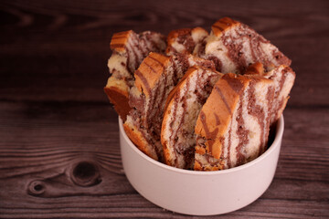 close-up of a bowl filled with freshly sliced marble cake revealing intricate swirls of chocolate and vanilla against a rich, textured wooden background evoking warmth and indulgence, cut, homely