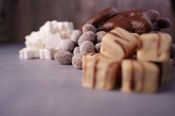 a close-up of assorted sweets: chocolate-covered treats, white marshmallows, and cocoa-dusted truffles displayed on a matte grey surface in a warm, soft light setting, decorative, treat, sweetness