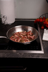 pan-frying bacon on an electric stove with fresh tomato and pepper garnish in a modern kitchen setting featuring a stainless steel pan, cuisine, sizzling, crispy, brown, dining, eat, plate, circle