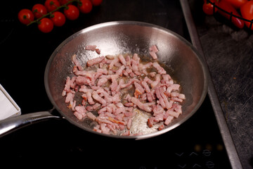 sizzling bacon strips frying in stainless steel pan with juicy tomatoes nearby against dark kitchen countertop, dinner, weekday, homemade, mealprep, slice, fresh, pantry, spice, seared, glossy