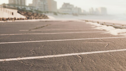 A tranquil morning unfolds as sunlight bathes an empty seaside parking lot, while soft waves lap gently at the shore, evoking serenity and calm in the early hours.