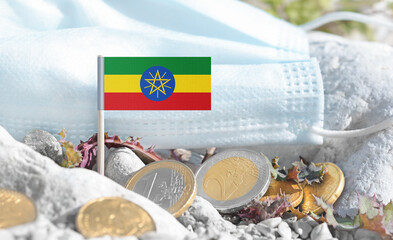 Ethiopian flag with euro currency coins and a medical mask on rocky ground.International healthcare costs,cross-border medical funding,Europe–Ethiopia cooperation and global health finance.