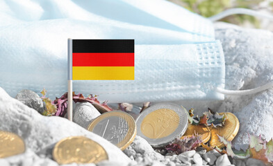 German flag with euro currency coins and a medical mask on rocky ground.Eurozone healthcare costs,medical funding challenges and the financial weight of modern services connected to Germany