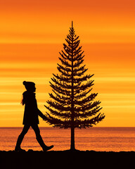 Silhouette of Woman Walking by a Christmas Tree at Sunset on the Beach 