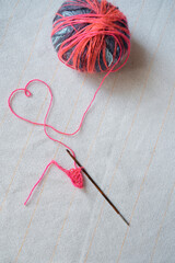 ball of colorful pink yarn and crochet hook flat lay on table