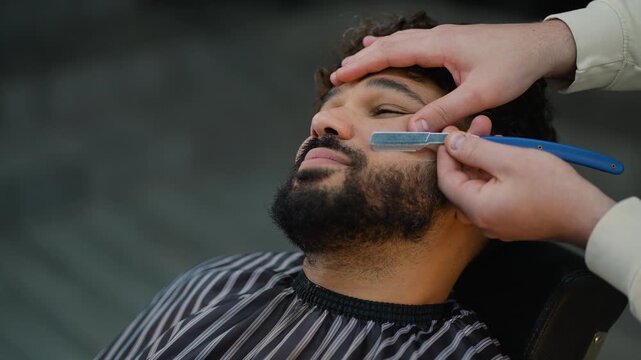 Professional barber shaping beard with straight razor