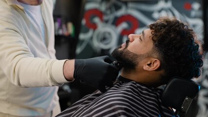 Barber trimming and shaping Arabian man's beard with an electric clipper