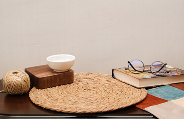 Cozy interior staging setup for product mock-up. Featuring an empty white bowl on a wooden riser, twine, and materials on a rustic woven mat. Perfect for product promotion.