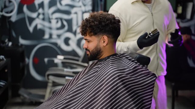 Professional barber giving haircut to male client with electric clipper