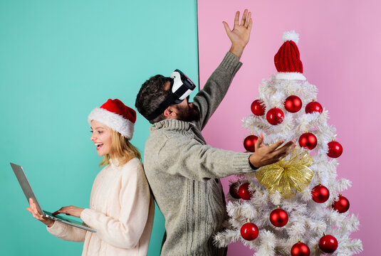 Happy couple at Christmas. Smiling woman in Santa hat with laptop and bearded man in VR glasses near Christmas tree. Family preparing for Christmas, New Year holidays. 3d technology, virtual reality.