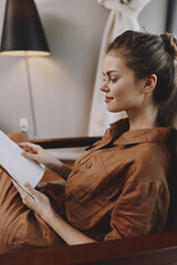 Young woman reading a book in a cozy, modern interior, wearing a brown linen dress, smiling, with warm light and soft colors creating a relaxed atmosphere