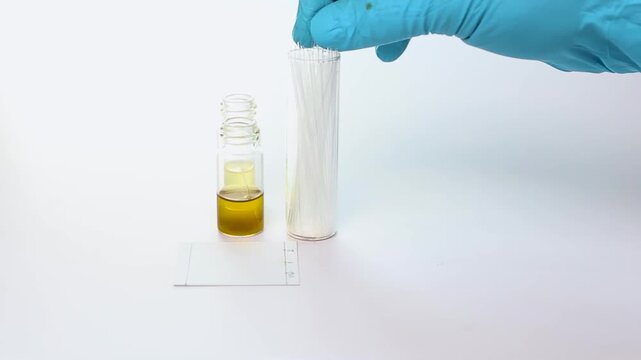 A scientist holds a capillary tube used for spotting chemical sample solutions onto a Thin Layer Chromatography (TLC) plate for chemical separation analysis.