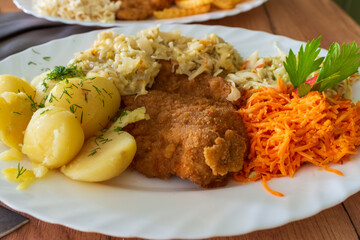 A breaded cutlet served with boiled potatoes, creamy cabbage salad, and shredded carrot. A hearty homemade meal presentation ideal for comfort food, traditional cuisine, and restaurant menu visuals.