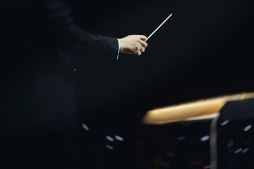 Male conductor behind the podium directing orchestra on stage with pupitre, musicians and choir,...