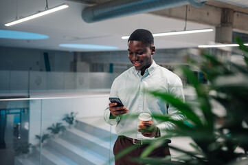 Young black man checking smartphone and holding coffee