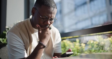 Man Contemplating Over His Phone at a Cafe Table in Natural Light with City View - Powered by Adobe