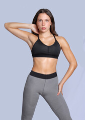 Young fitness athletic woman wearing blue legging and black top posing touching her neck and legs looking at camera with determination discipline expression stand on grey background