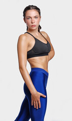 Young fitness athletic woman wearing blue legging and black top posing touching her leg looking at camera with determination discipline expression stand on white background