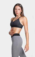 Young fitness slim athletic woman touching her abdominals wearing grey leggings and black top looking at camera isolated on white background, determination expression to keep training