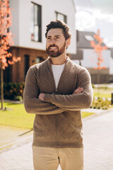 Confident handsome Latin man with beard standing in suburban neighborhood looking away
