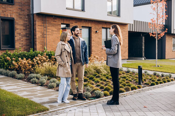 Happy couple interacting with realtor outside modern new house on the street