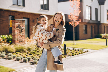 Happy, smiling, beautiful mother holding daughter smiling outdoors residential area
