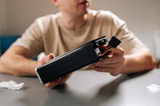 Cropped shot of technician working with electronic device, holding computer hardware with exposed cooling fan, performing repairs and maintenance on tech equipment in modern workshop environment.