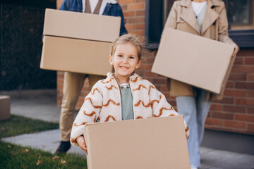 Happy family moving into new home carrying cardboard box little cute girl looking at camera