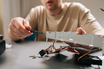 Closeup shot of technician male performing computer repair, using screwdriver to fix open electronics hardware, servicing device components at workbench. Concept of technical support and maintenance.