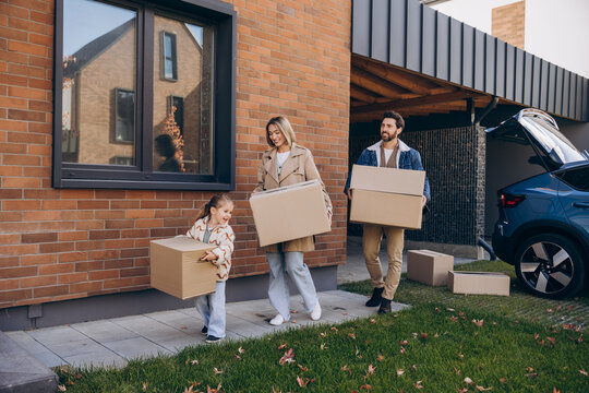 Smiling happy family moving into new house carrying cardboard boxes - Powered by Adobe