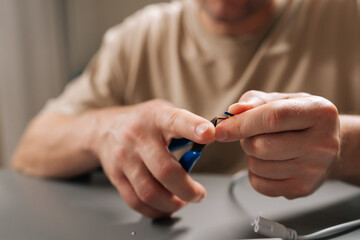 Close-up of male hands fixing damaged electrical cable at workbench, stripping outer insulation with wire stripper tool, performing diy repair on electronics and home appliances.