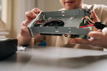 Closeup of unrecognizable repairman completing electronic repairs in bright workshop, holding disassembled hardware, exposing intricate internal components and ensuring proper functionality.