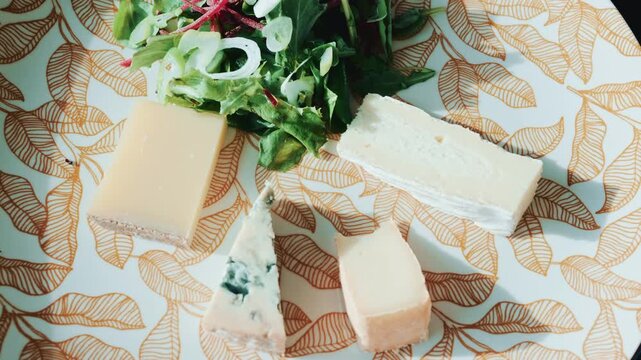Close up of a cheese plate with assorted cheeses and salad on an elegant patterned plate