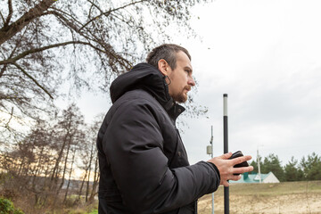 man in a city park with a phone wearing a black jacket in cloudy autumn weather