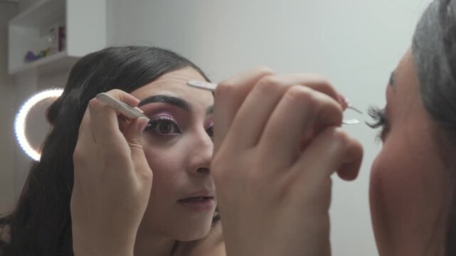 Behind-shoulder view of girl attaching false eyelash with precision
