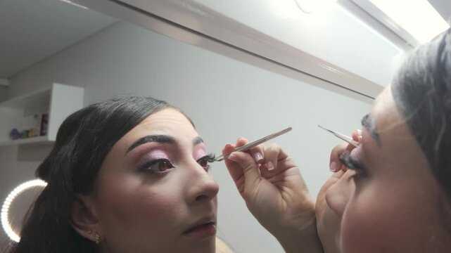 Young model applying false eyelashes carefully before mirror lights