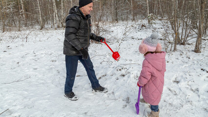 Little girls with her grandfather walk in a snowy forest, have fun together