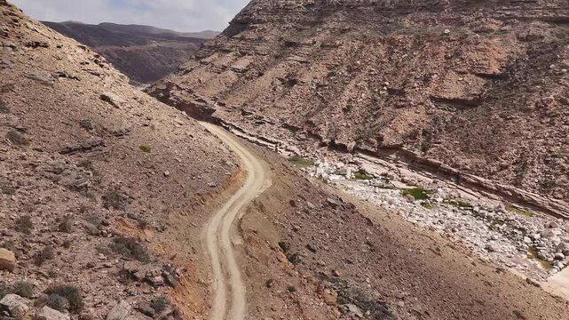Aerial view of driving cars in dry valley in the island of Socotra. Motion drone video of moving cars on bumpy road surrounded by stones and dessert plants. Following cars from the air. Off-road drive
