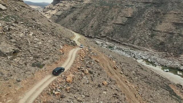 Aerial view of driving cars in dry valley in the island of Socotra. Motion drone video of moving cars on bumpy road surrounded by stones and dessert plants. Following cars from the air. Off-road drive