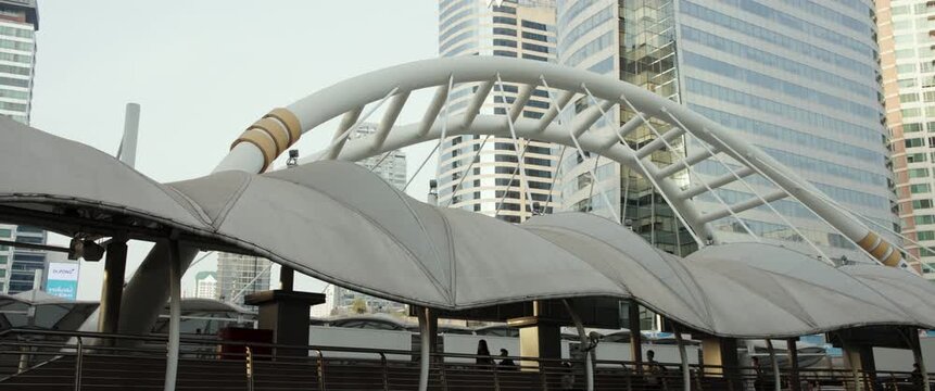 Bangkok, Thailand - 11.02.2024: Futuristic Chong Nonsi skywalk with pedestrians and decorative arch against skyscrapers in Bangkok anamorphic lens. Long footbridge connecting urban districts