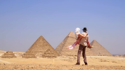 Man lifting a woman as they enjoy a romantic moment in front of the pyramids during their Egypt vacation.