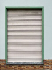 closed window with shutters, green wall with rolled up jalousie, and a part of a brick wall 
