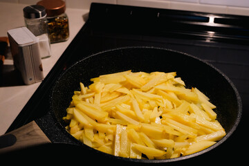 Sliced potatoes cooking in a frying pan on a stovetop in a home kitchen, preparation of a simple...