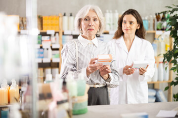 Elderly woman chooses pills for headache and allergy and consults with a pharmacist about the choice of medicines in a European pharmacy. Woman buys high-quality European medicines